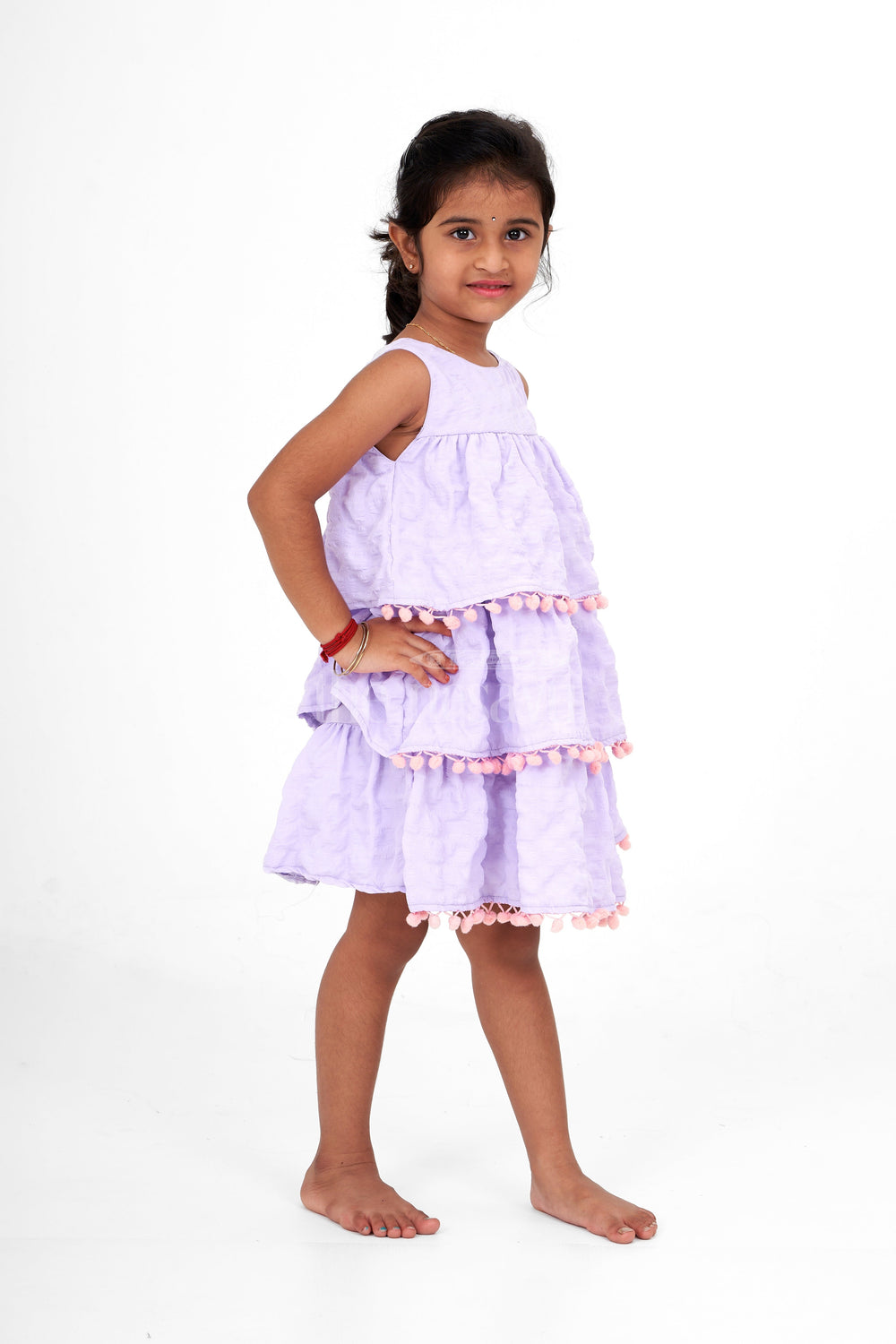 The Nesavu Girls Fancy Frock Lilac-Tiered Girls Fancy Frock with Pom-Pom Trim and Sleeveless Design for Parties Nesavu Nesavu Lilac-Tiered Girls Fancy Frock Pom-Pom Trim Textured Fabric Birthday Parties